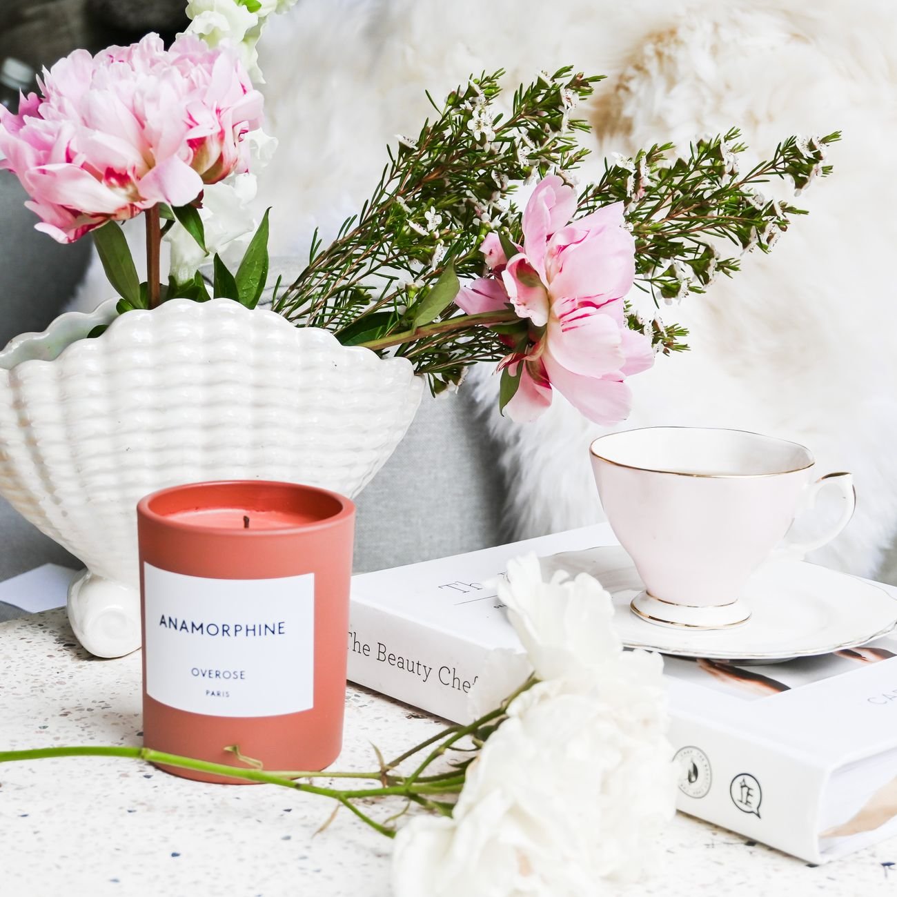 Charming still life with flowers, candle, teacup, and book for serene home decor.